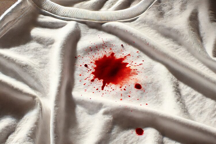 DALL·E 2024-10-24 16.58.14 - A close-up image of a white t-shirt with a small blood spot. The blood spot is irregular in shape, contrasting vividly against the clean, bright white